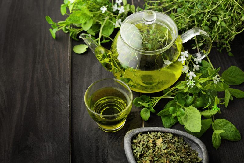 A glass tea pot, a glass and some tea leaves with green tea