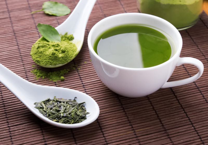 A mug of green tea, a spoon of matcha powder and green tea leaves