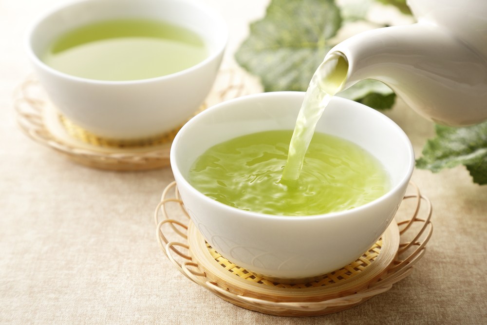 Two white bowls of green tea with tea being poured into them