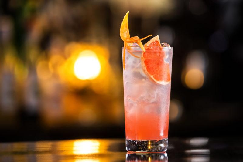 An in-focus image of a Greyhound cocktail with ice, in front of an out-of-focus bar