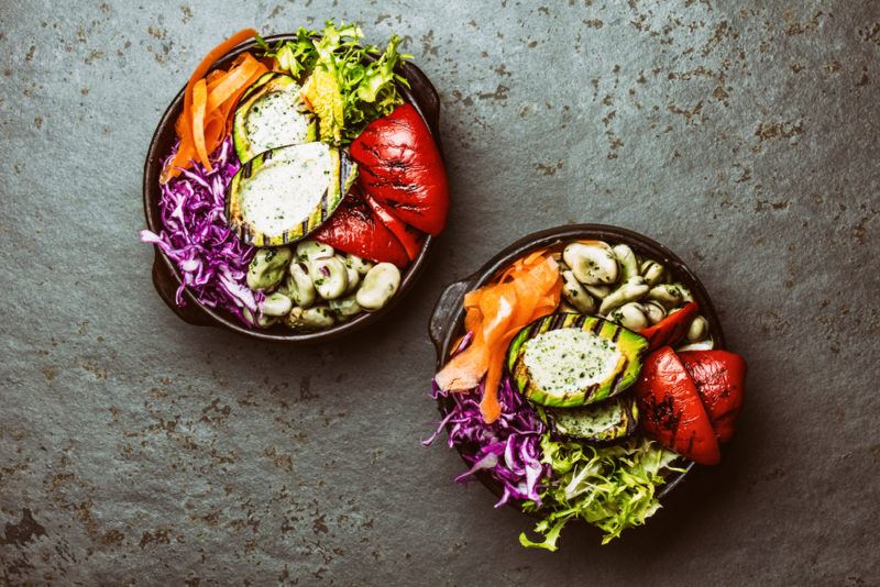 Two black bowls with healthy ingredients, including grilled stuffed avocados