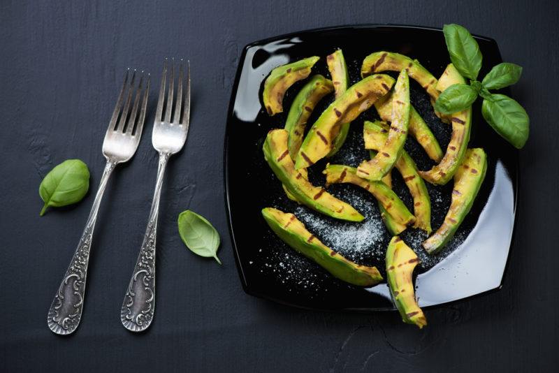 A black plate containing grilled avocado that has been sliced