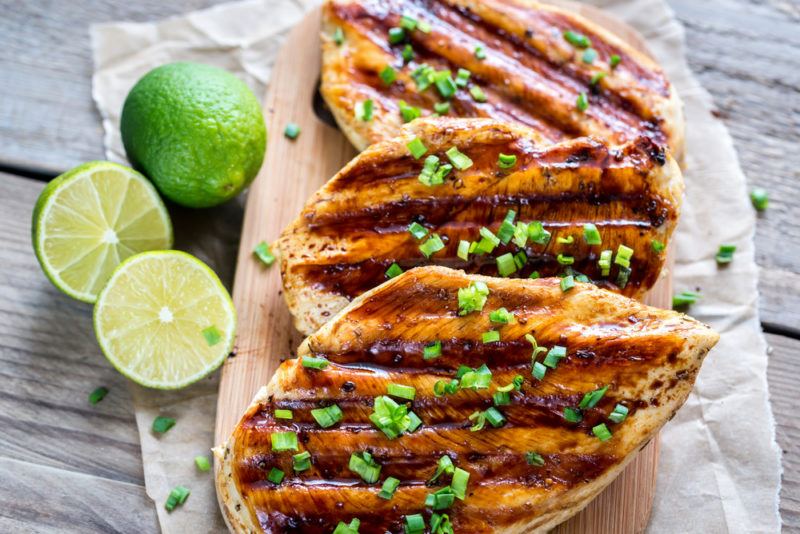 Grilled chicken with lime | Food For Net A wooden board with three pieces of grilled chicken next to limes