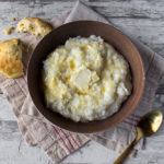 A brown bowl of grits next to a spoon