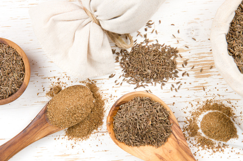 top view image of wooden spoons, bowl, and sack full of whole and ground cumin