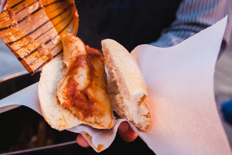 Someone in the street holding a guajalota, which is a Mexican dish that involves a tamele in a sandwich