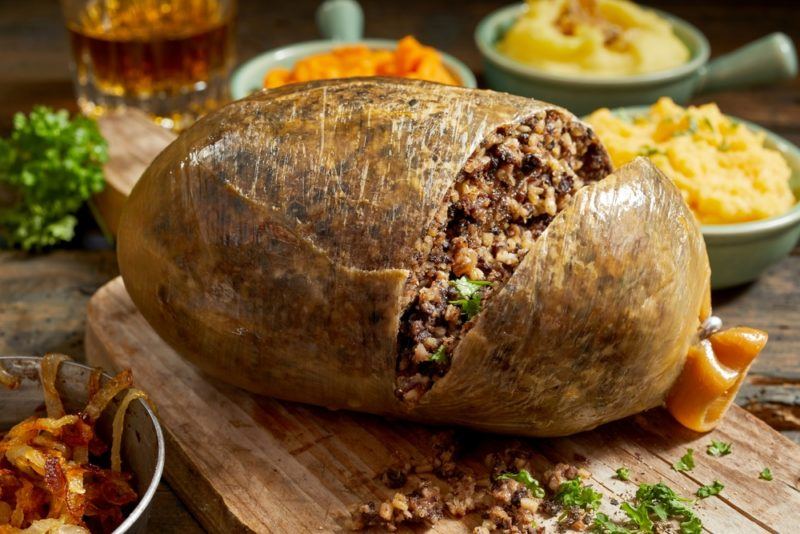 A haggis that has been opened on a board with breakfast foods in the background