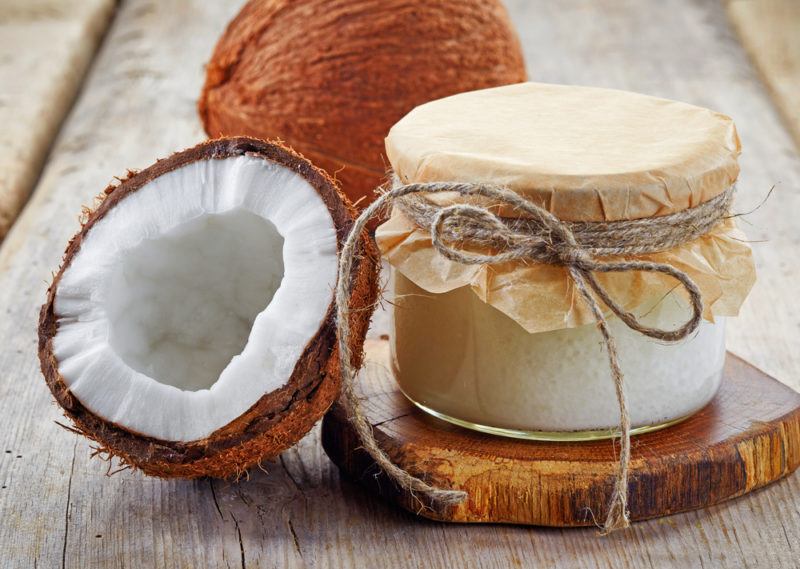 A jar of coconut oil next to a full coconut and a coconut half