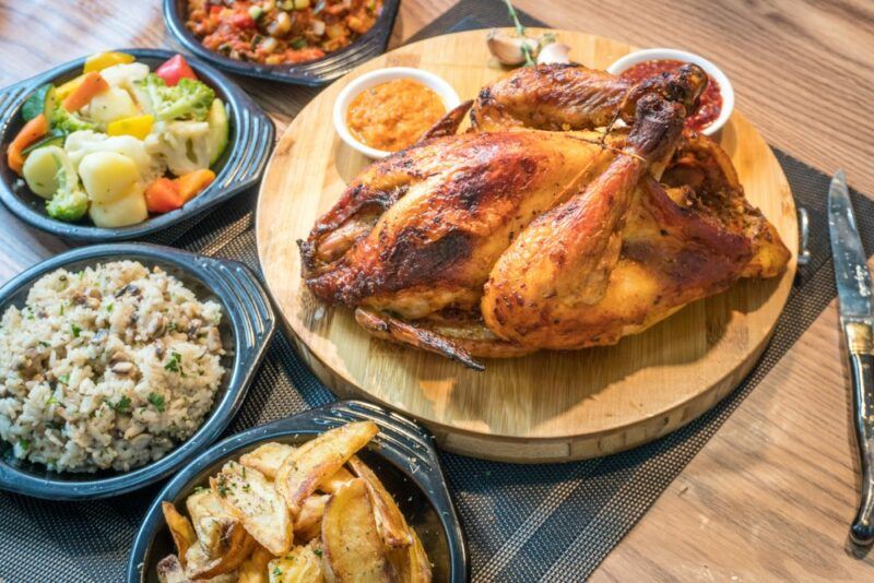 Half a rotisserie chicken on a wooden board, next to a selection of sides, like coleslaw