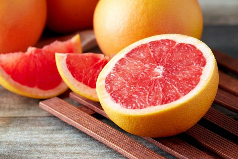 A whole grapefruit and one that has been cut in halve and into wedges on a wooden table