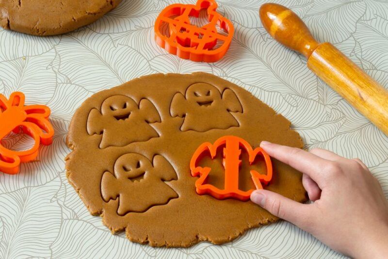 Brown cookie dough with four ghost cookies being cut out of it using an orange cookie cutter