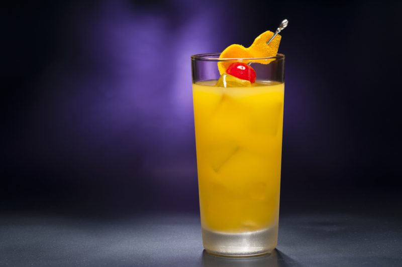 A tall Harvey Wallbanger cocktail against a purple background