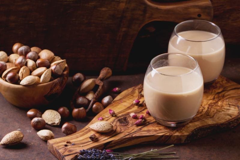 Two glasses of hazlenut milk on a wooden board next to hazelnuts