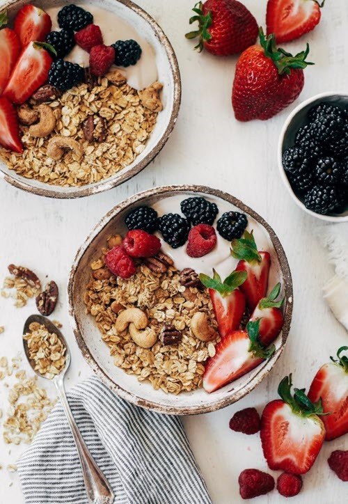 Two bowls containing healthy homemade granola, surrounded by berries