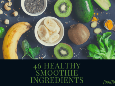 A selection of fresh smoothie ingredients on a black background, including kiwi, bananas, chia seeds and greens