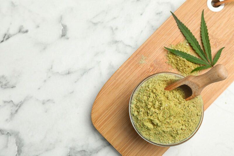 A marble table with a wooden board, a bowl of hemp protein powder and a scoop