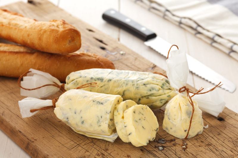 A wooden board with herbed butter, next to some bread sticks