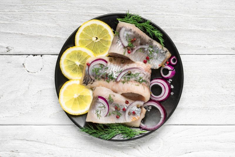 A black plate with herring fillets and lemon slices