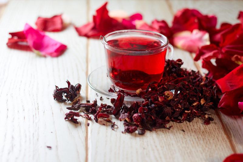 A glass of hibiscus tea on a wooden table with dried and fresh hibiscus flowers