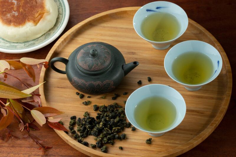 a wooden tray with 3 tea cups with a tea pot with loose Gaoshan or High Mountain Tea beside it