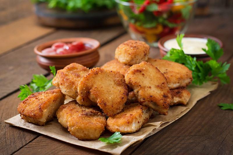 A dish of homemade chicken nuggets, with a small container of tomato sauce in the background