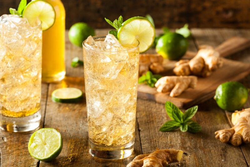 Two glasses of fresh ginger ale with ice on a table, with some ginger and limes