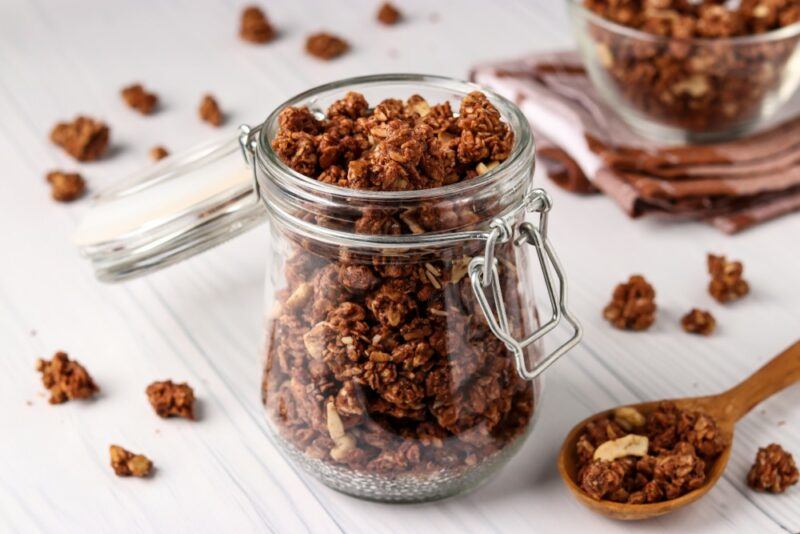 A glass jar containing homemade granola, with more scattered across the table