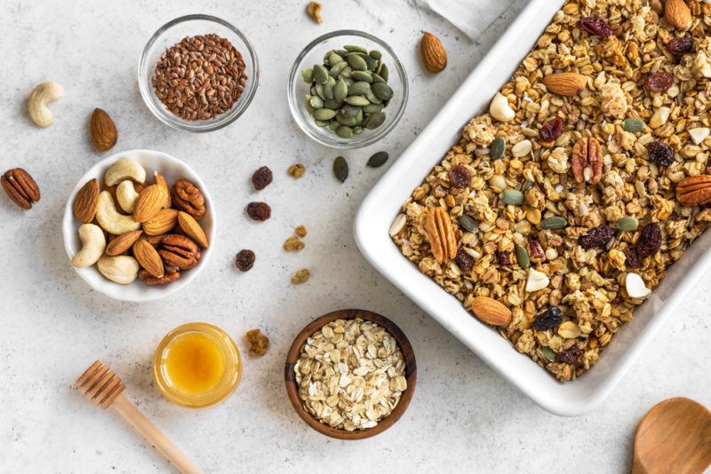 A white pan of granola, with ingredients like seeds and oats on their own in bowls too