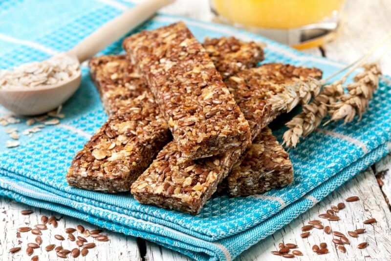 A light blue towel with a pile of homemade oatmeal bars, next to a wooden spoon containing oats