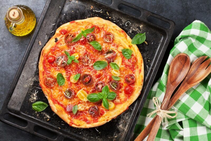 A fresh homemade pizza with red sauce, meat, and greens