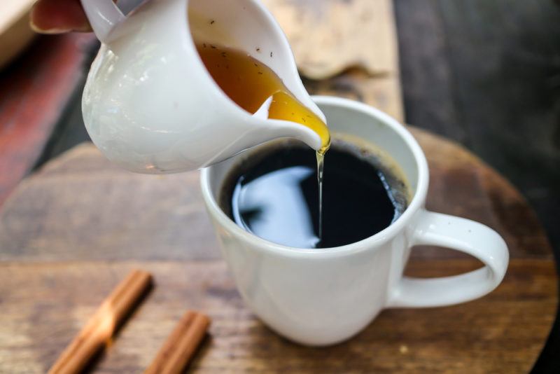 Honey being poured from a white jug into black coffee