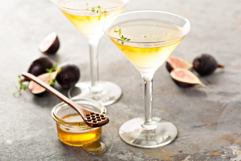 Two honey cocktails in cocktail glasses with figs and honey next to them