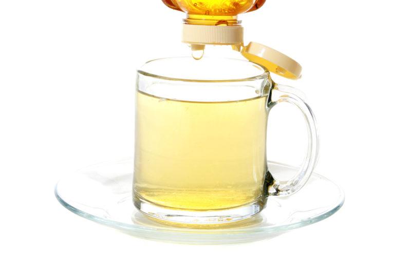 A glass of honey and hot water with honey being dripped into it