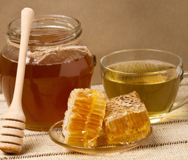 A jar of honey and a plate containing honeycomb, next to a glass bowl of honey water