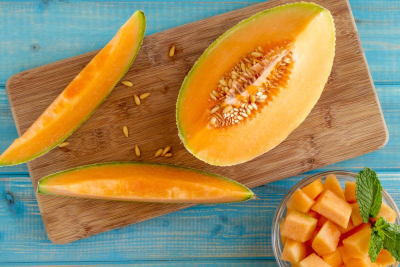 A wooden board with a honeydew melon and a couple of slices