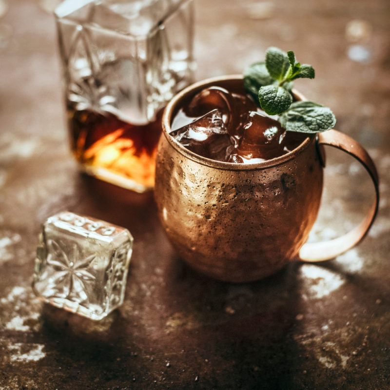 A horsefeather cocktail in a copper mug, with a decanter of whiskey next to it