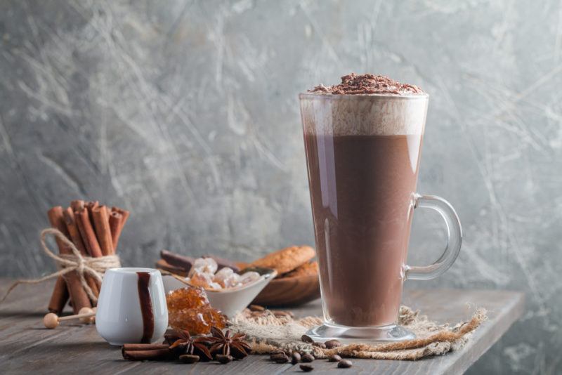 A tall glass mug with hot chocolate, cream and cinnamon