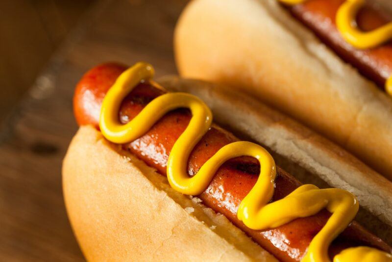 A close up image of two hot dogs with a line of mustard on each