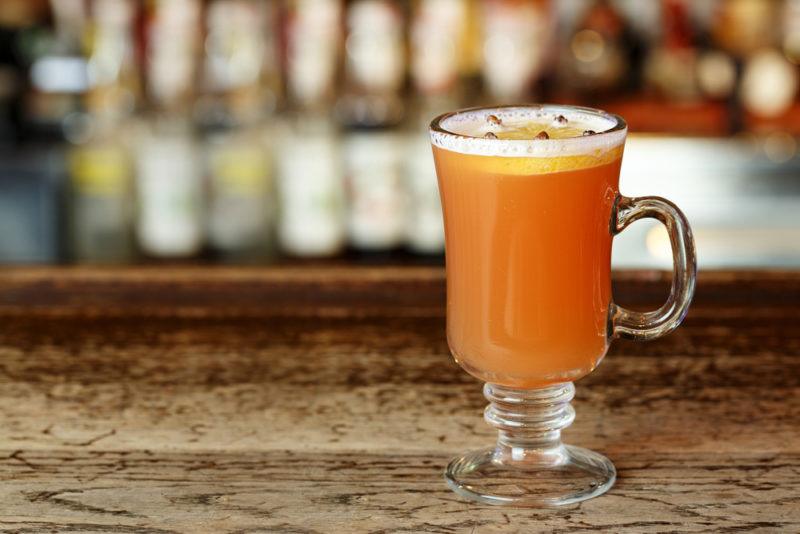 A glass mug containing a hot toddy in front of a bar