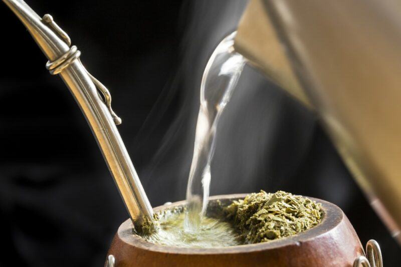 A jug of hot water pouring into a gourd of yerba mate with its metal straw