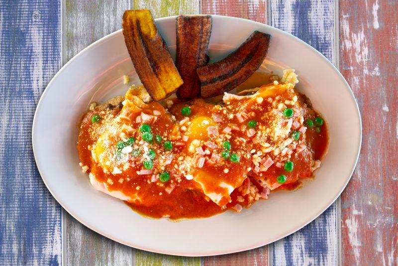 A white plate with Huevos Motulenos, which is a Mexican dish that is often served with plaintains or bananas