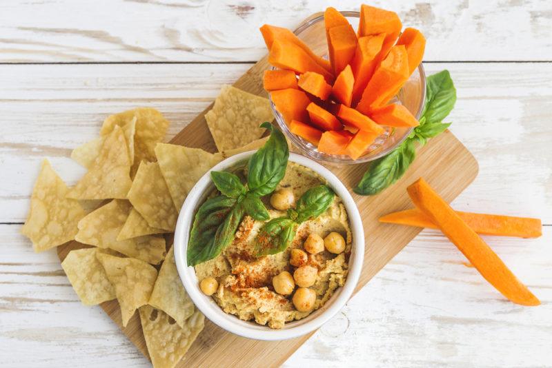 Hummus, crackers and carrot sticks on a wooden board