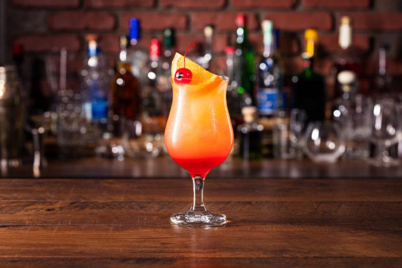 A Hurricane cocktail in focus with a bar in the background