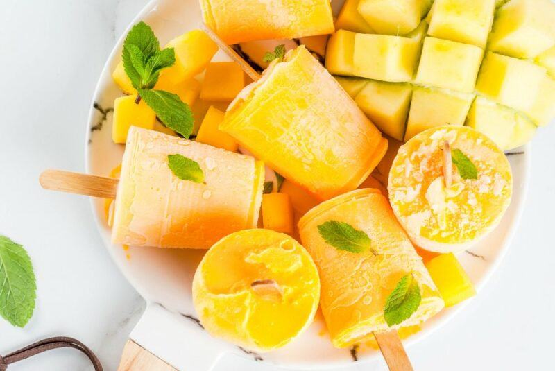 A large white bowl with mangos and mango popsicles