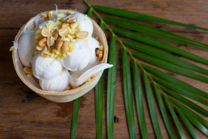 A bowl of coconut ice cream with nuts on top, next to a coconut frond