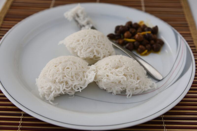 a white dish with Idiyappam noodles resting on a bamboo place mat