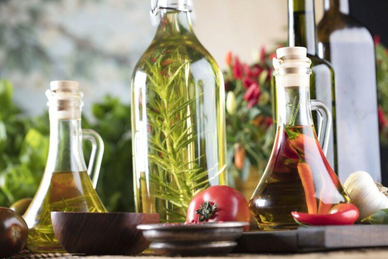 Bottles of freshly infused olive oil on a table, including rosemary, chili, and garlic as ingredients