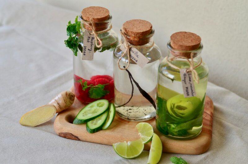 Three bottles of vodka on a wooden board, each with a different type of ingredient, including berries, vanilla and lime. There are more ingredients in front