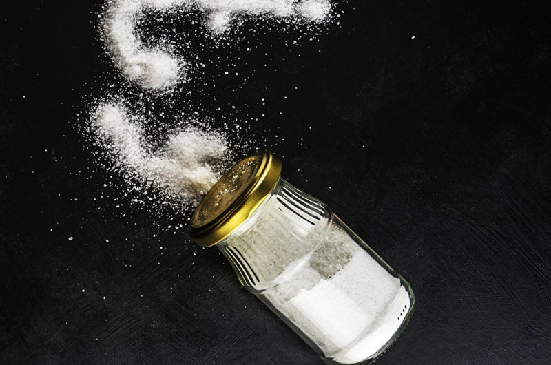 A shaker of iodized salt being spilled out onto a black table