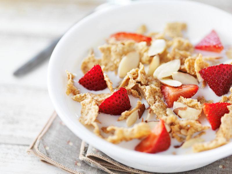 A white bowl containing cereal and sliced strawberries